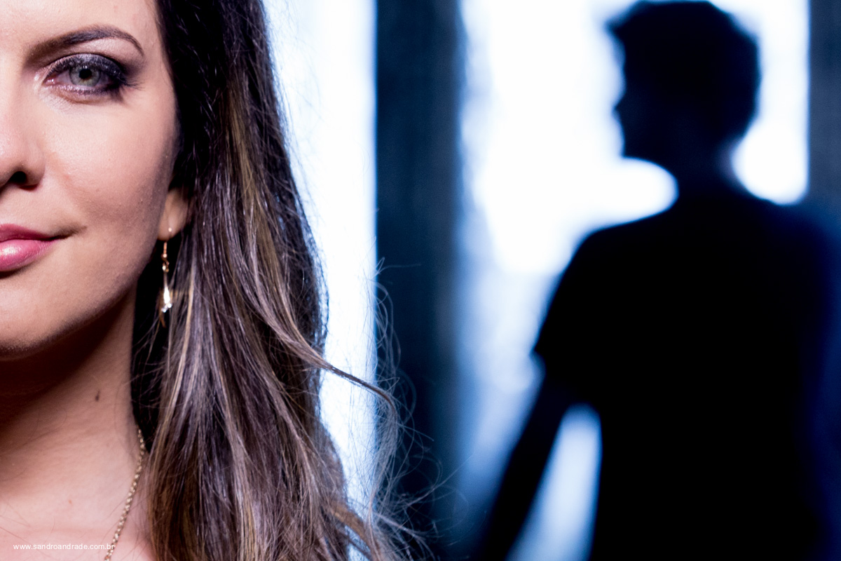 Ele em silhueta no fundo da fotografia e metade do rosto dela com esse belo olho verde em destaque. 