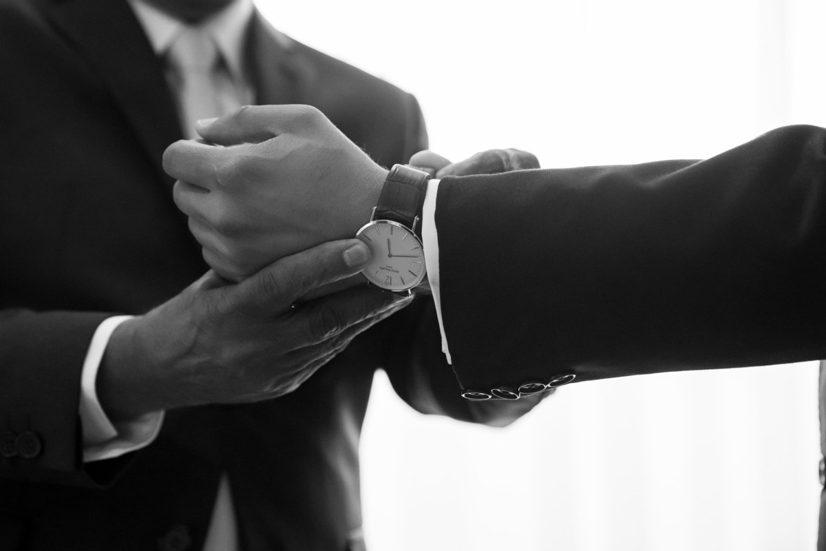 Mais detalhes, as mãos do pai do noivo fechando relógio de seu filho no pulso dele.