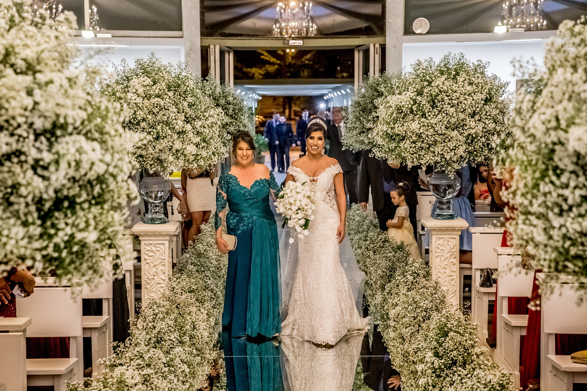 Ela entra na igreja de braço dado com sua mãe, emocionada e feliz em estar realizando seu sonho com o amor de sua vida.