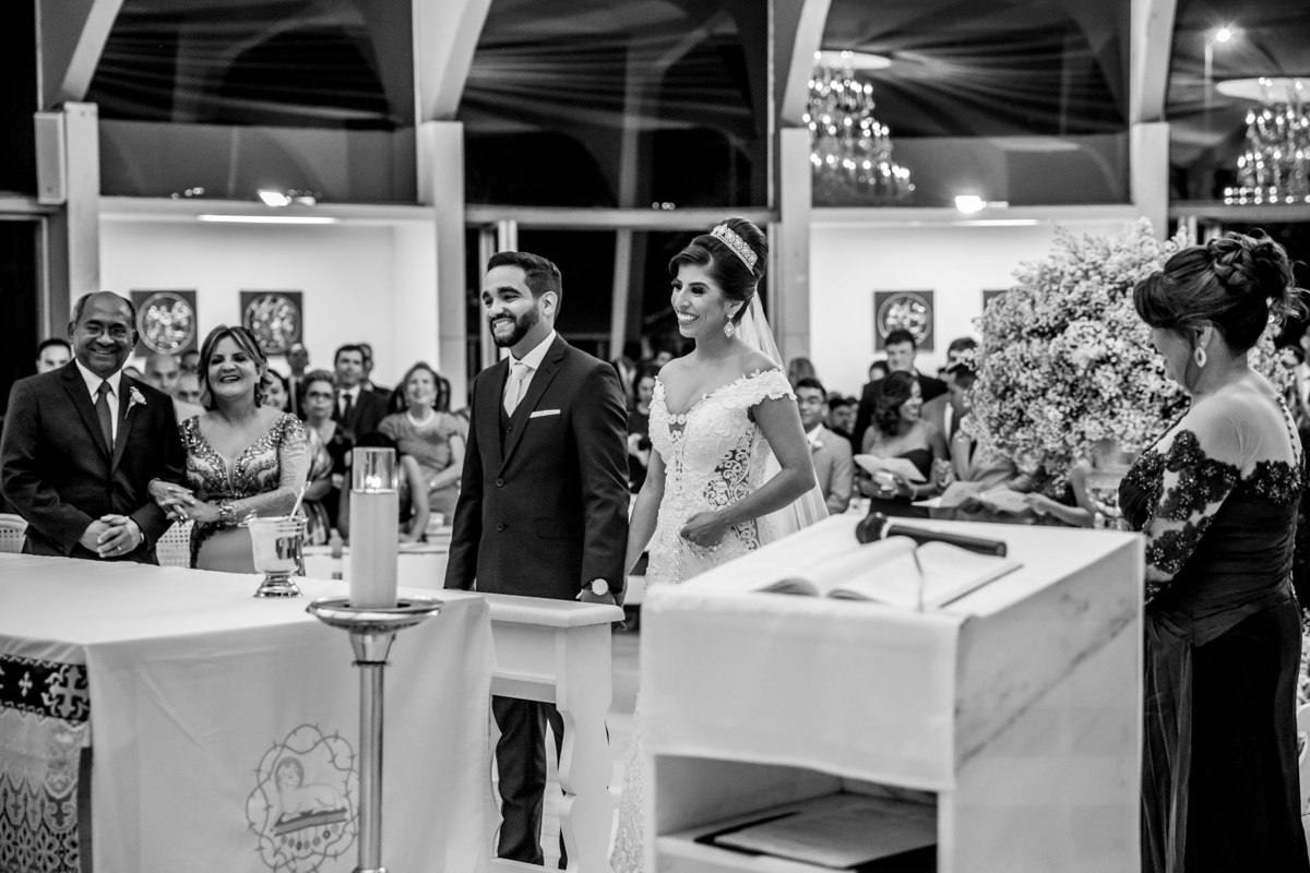 Uma fotografia preto e branco, após a entrada da noiva, ambos no altar com os pais do lado e todos felizes.
