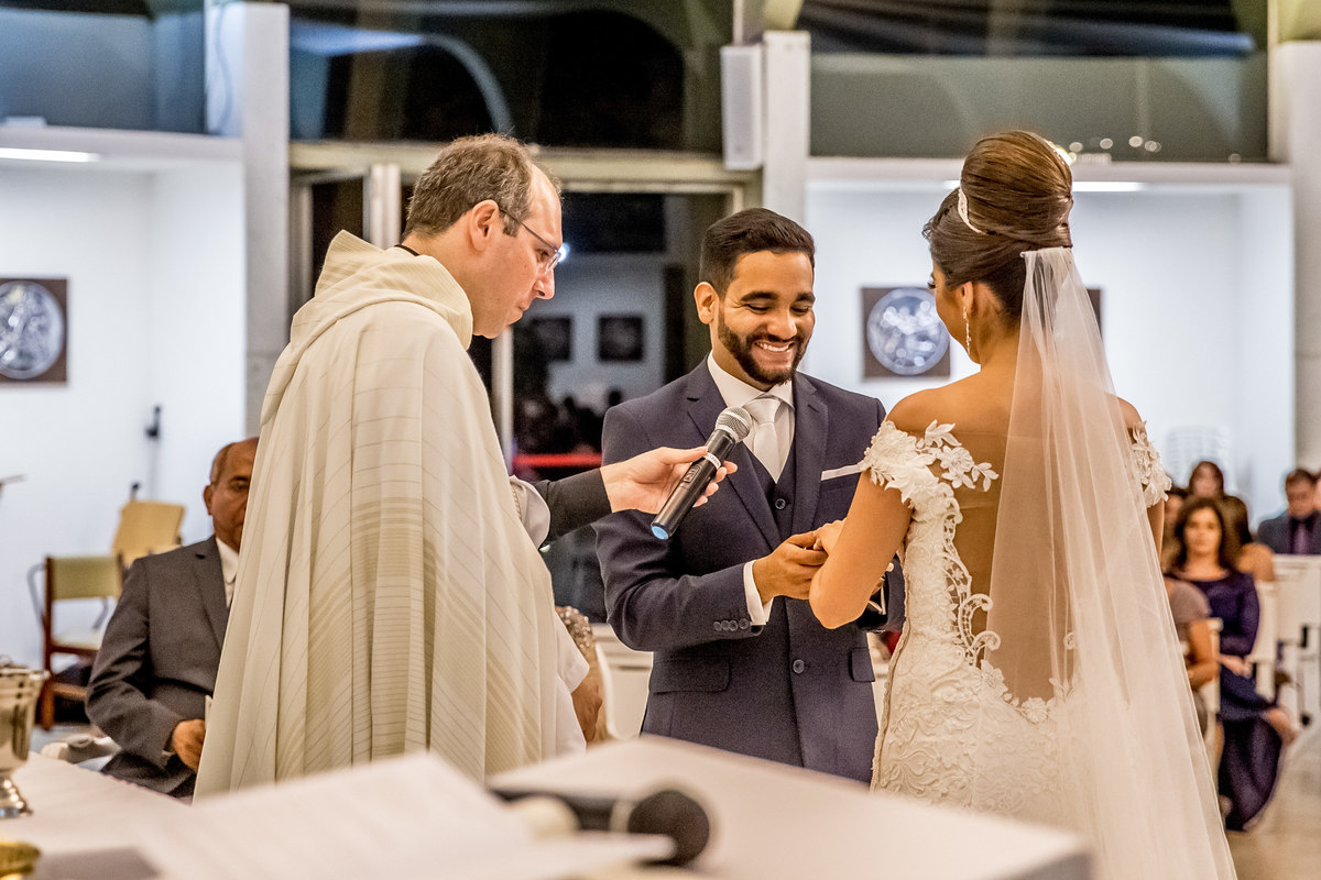 Apaixonado o noivo coloca a aliança no dedo de sua agora esposa.