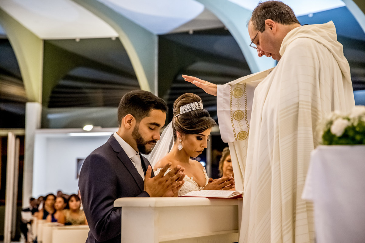 Benção final, o casal ajoelhados e o padre com a mão imposta sobre a cabeça dos dois abençoa o mais novo casal de Brasilia pelo olhar do fotografo Sandro Andrade, fotografo de casamentos.