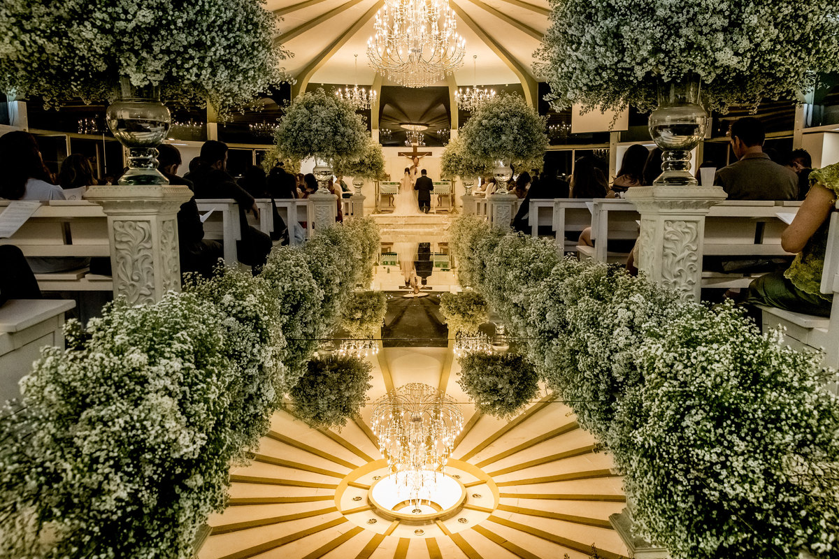 A igreja toda com sua glamurosa decoração e os noivos de costas, ajoelhados no altar.
