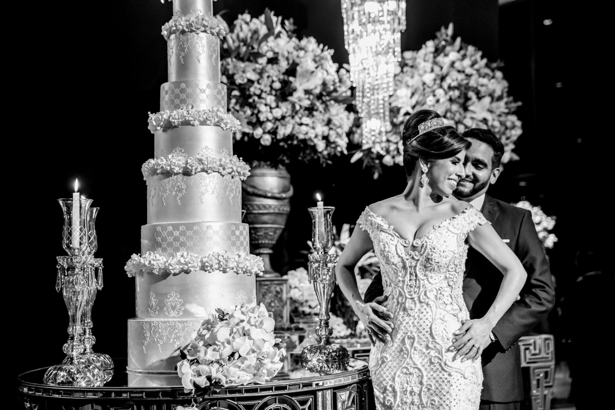 Em frente a mesa do bolo o casal posa para fotos, uma linda fotografia preto e branco. 