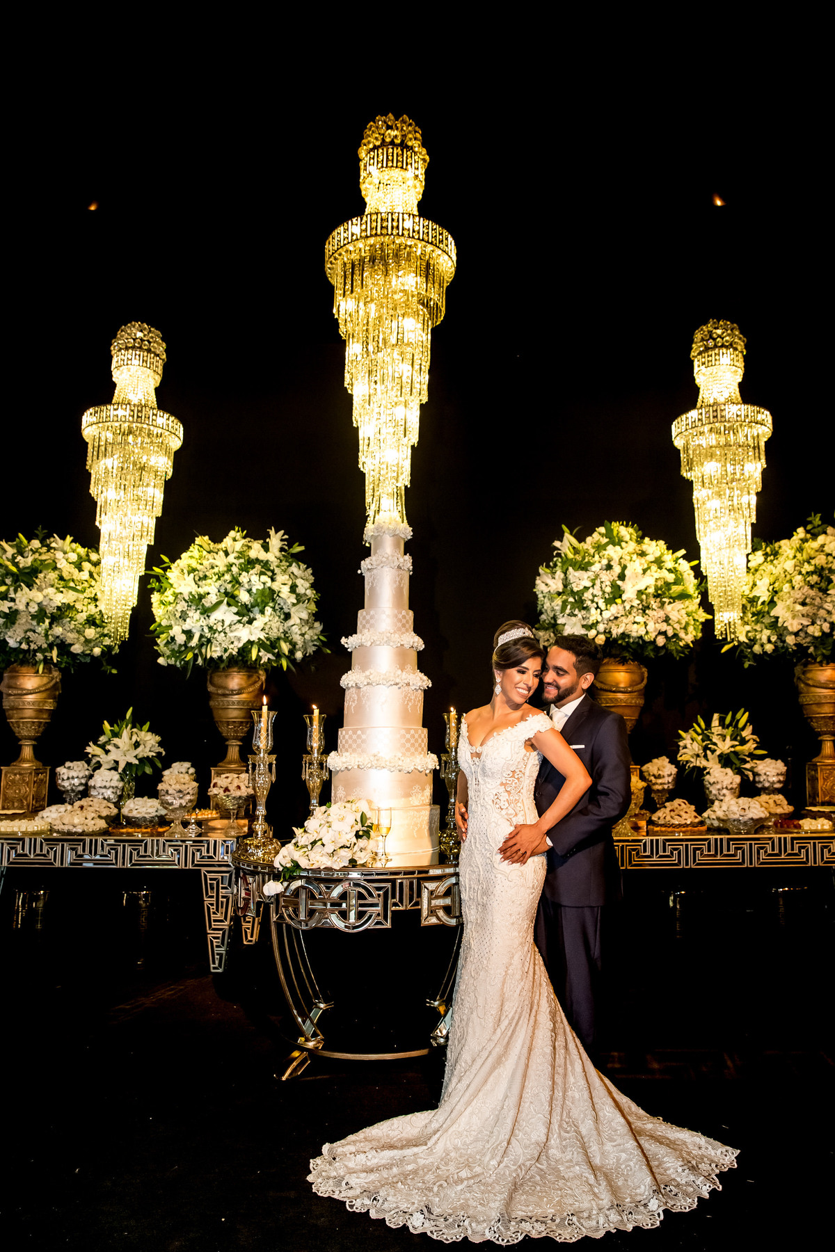 Esta fotografia clássica com os noivos juntinhos e o vestido da noiva com a cauda toda aberta, ao lado do bolo, ficou tão linda que o fotógrafo Sandro Andrade não resistiu, a emoldurou e colocou em uma linda ampliação de 2,00x1,00 metros.