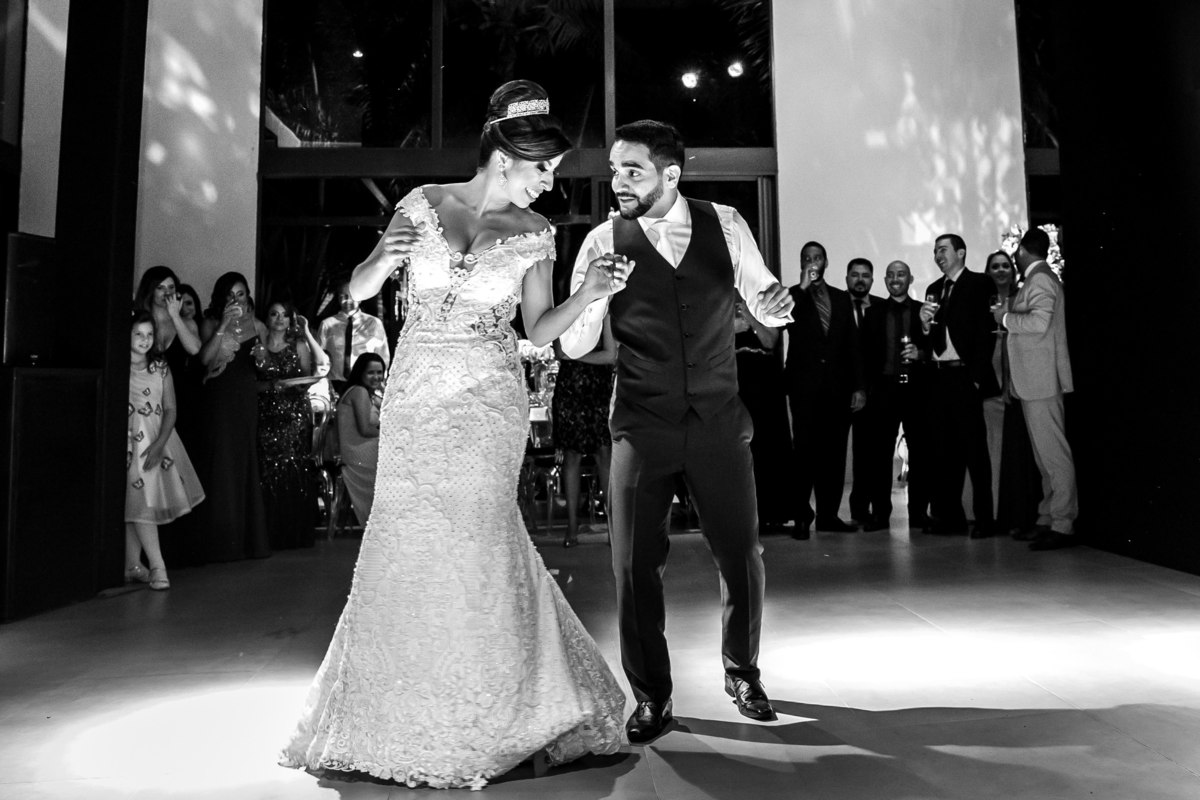 Os noivos dançam com os convidados ao fundo.