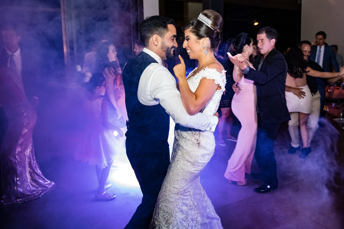Dançando agarradinhos na boate do casamento deles e com vários convidados ao redor.