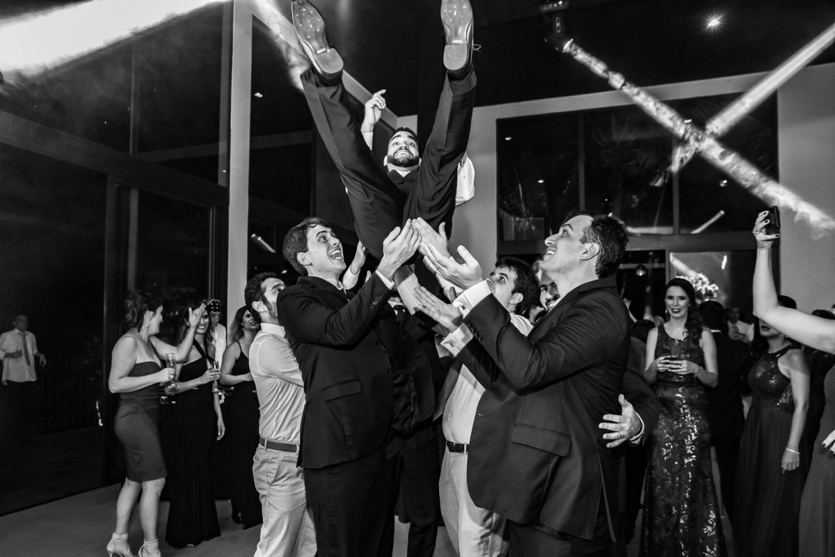 Os amigos do noivo o pegam e jogam ele para cima.