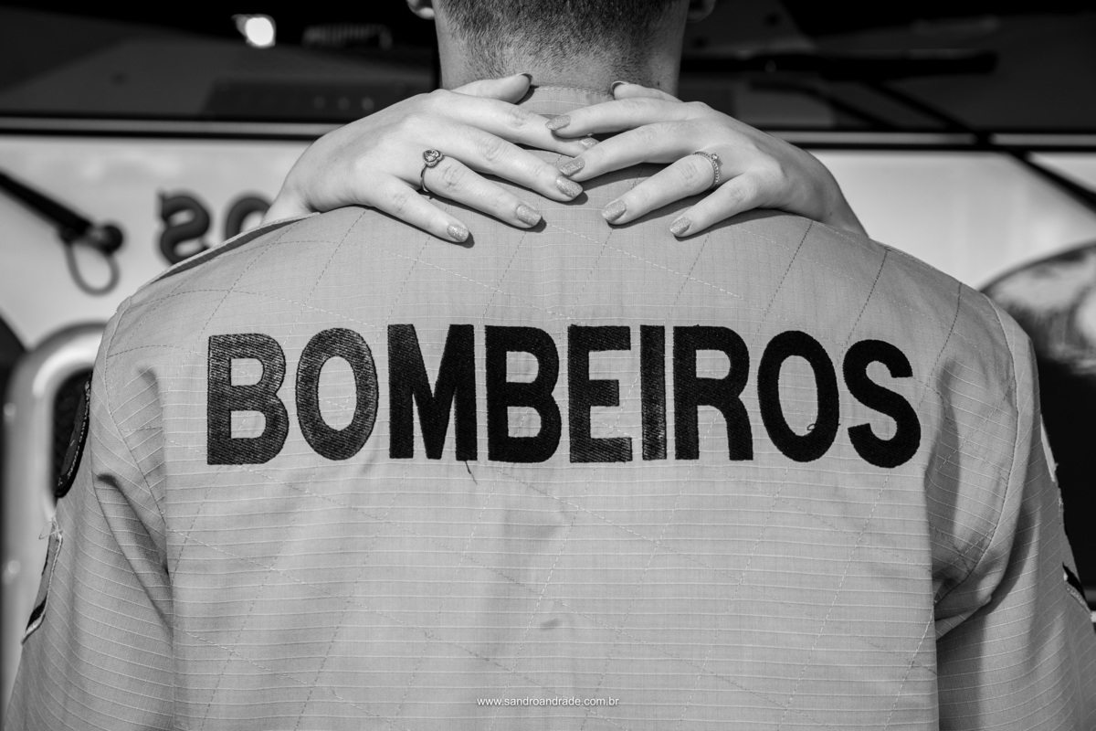 A primeira parte do ensaio de Hamanda e Michel foi feita no corpo de bombeiros, onde o noivo trabalha. Esta fotografia é o detalhe do uniforme do noivo onde aparece o nome BOMBEIROS e um pouco acima temos as mãos da noiva com seu anel de noiva.