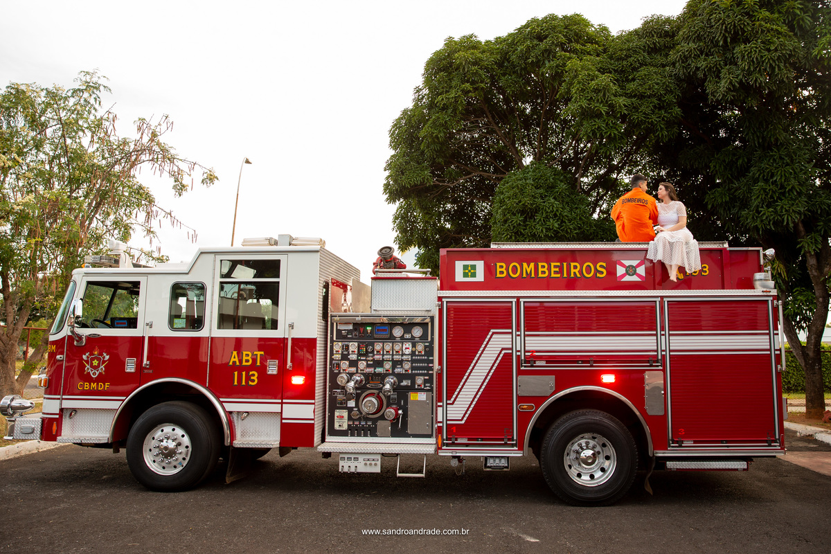 Os noivos sentados no topo do caminhão do corpo de bombeiros, ela de frente para o fotógrafo e o noivo de costas. Fotografia criativa do fotógrafo de casamento m Brasília. 