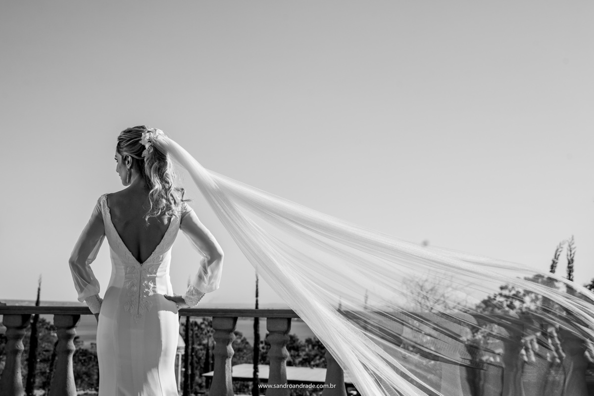 Em um belíssimo preto e branco, esta fotografia mostra os detalhes do vestido de costas, a noiva está de perfil olhando na direção da ponte JK.