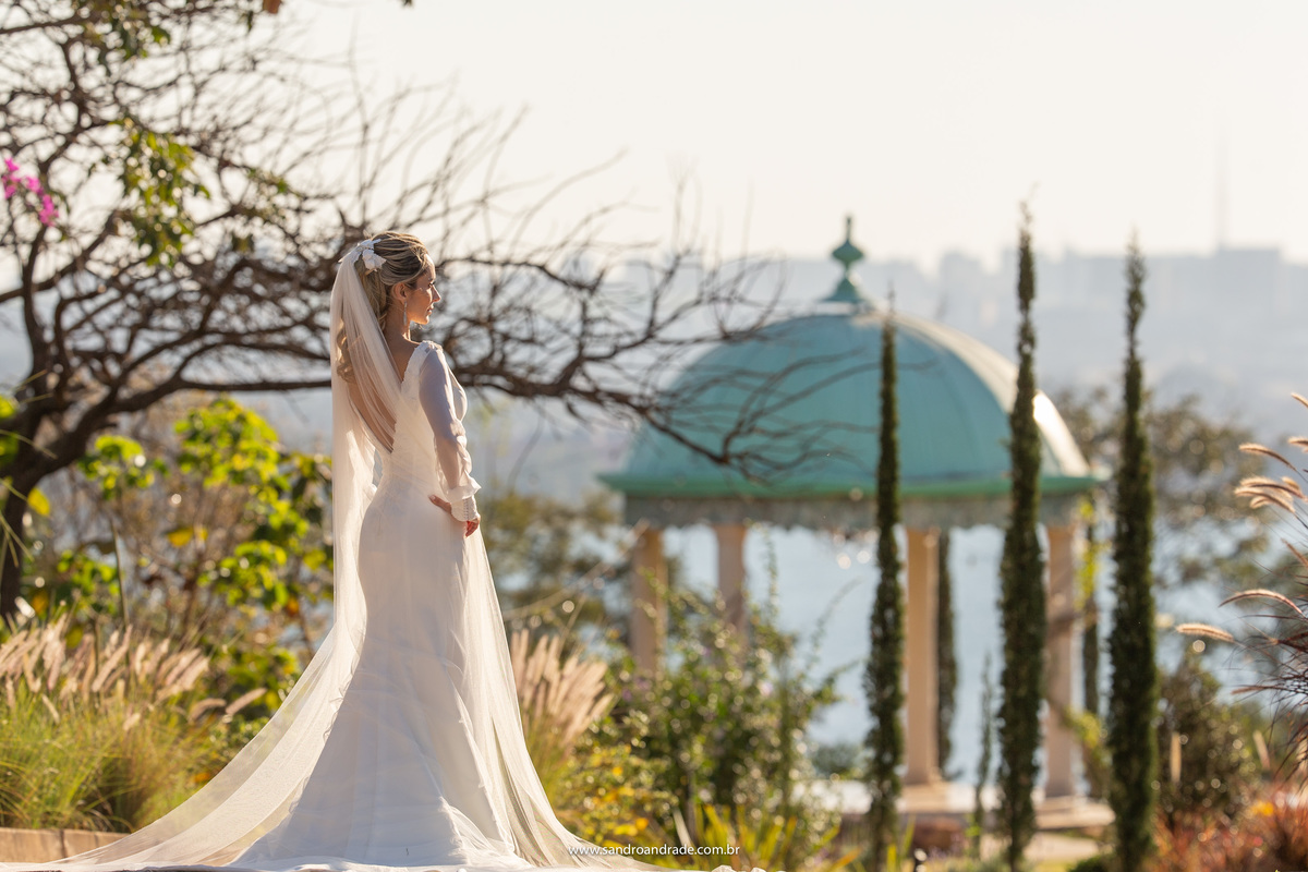 Com o gazebo de fundo, ponto marcante a Villa, a noiva está olhando para o horizonte.