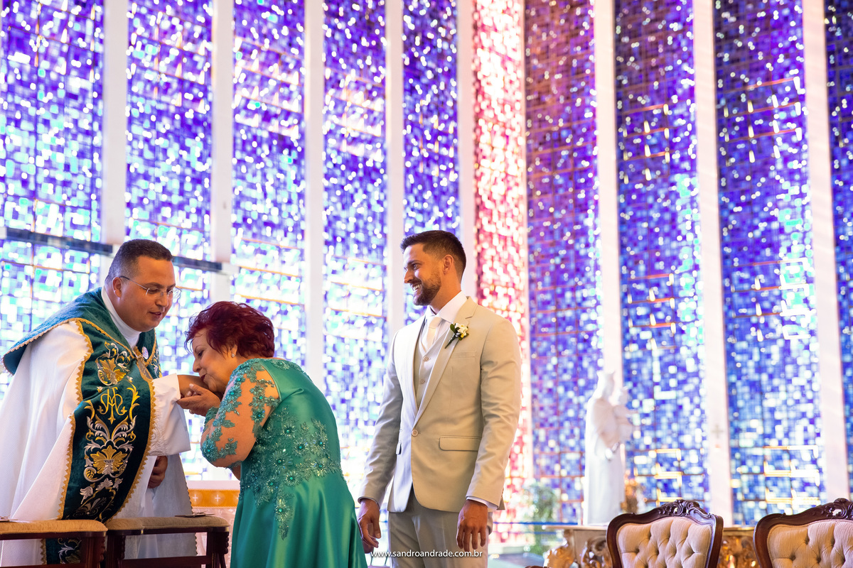 A mãe do noivo cumprimentando o padre de maneira muito carinhosa.