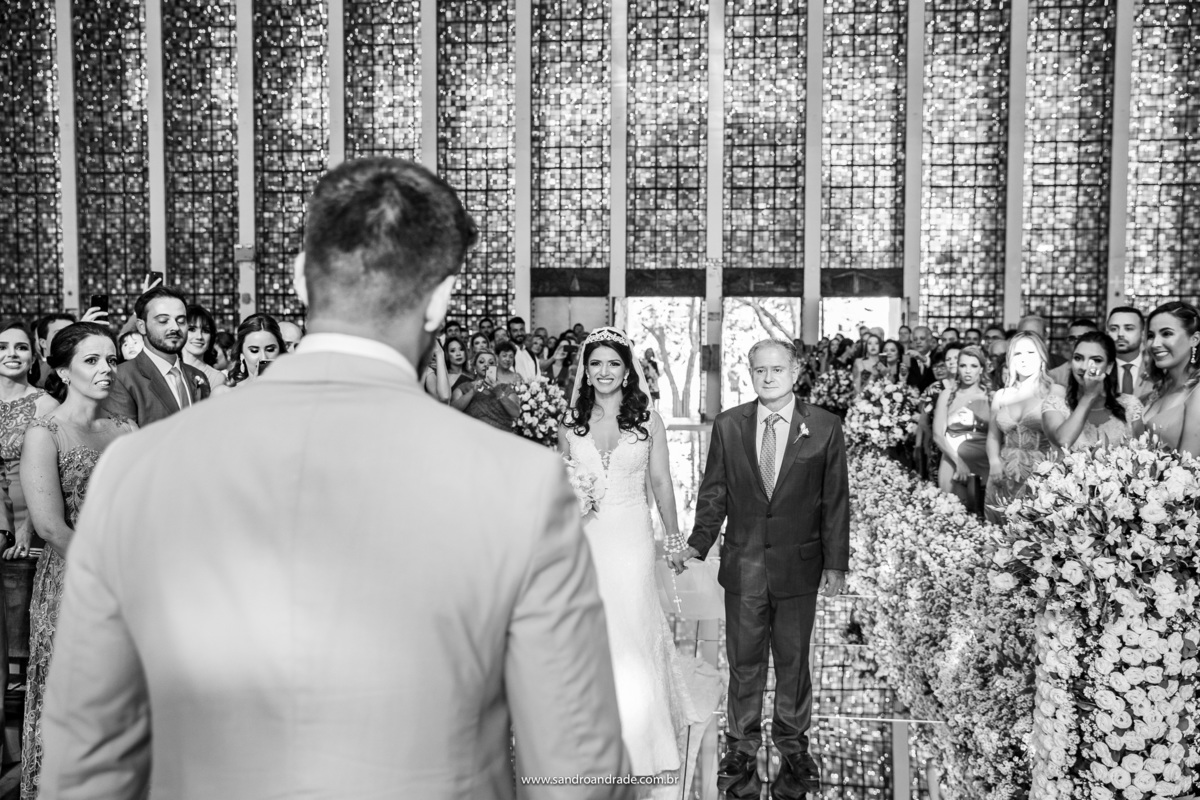 Emocionada ela e seu pai se aproximam do noivo.