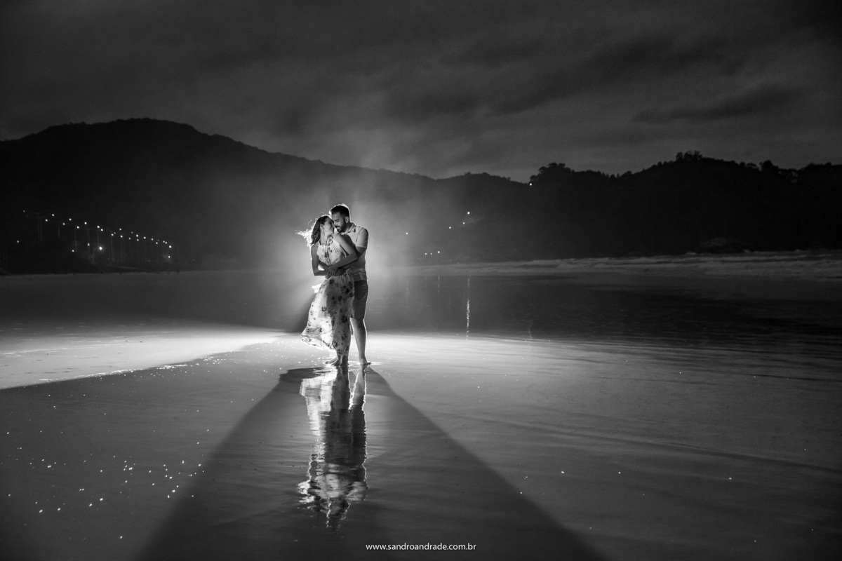 Ensaio fotográfico noturno sob a luz do luar na praia de Mariscal em Bombinhas - Santa Catarina. Fotografia do casal em preto e branco, agarradinho e paixonados, reflexo na areia da praia.