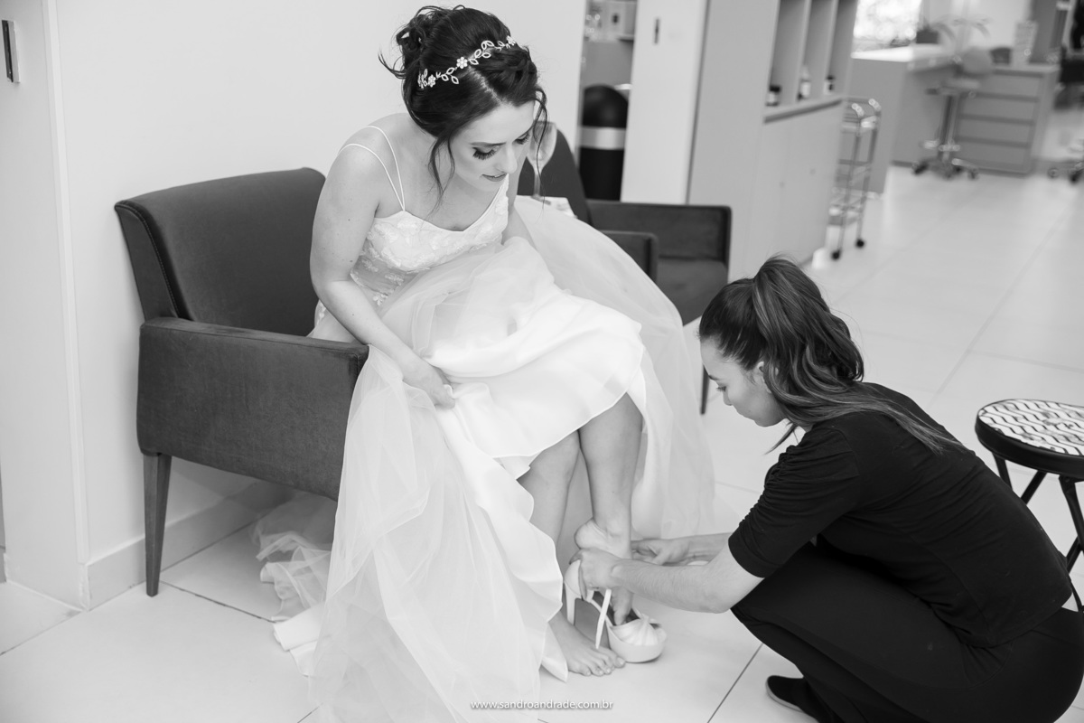 Se preparando para ir ao encontro de seu grande amor, a cerimonial está colocando o sapato no pé da noiva.