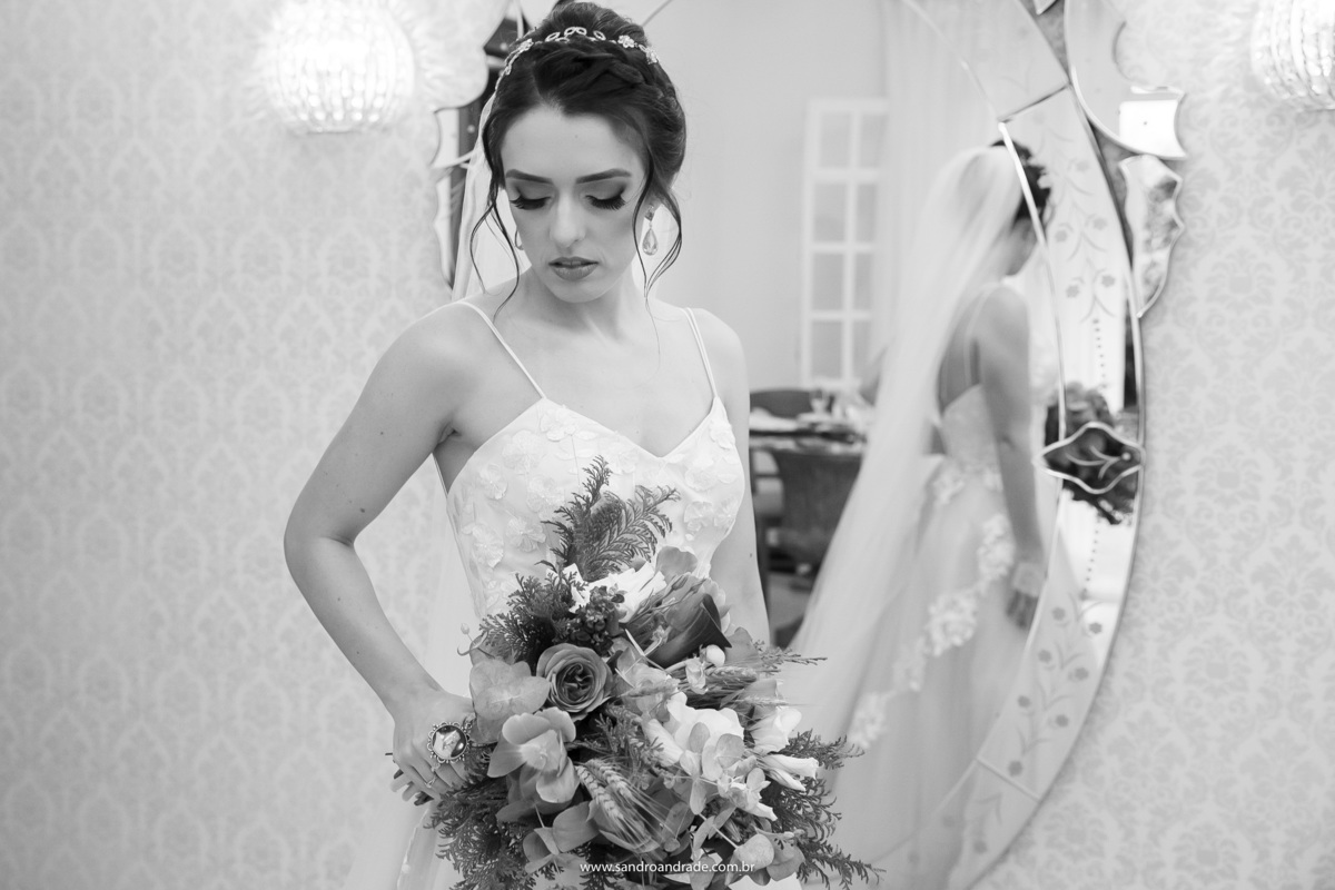 Uma fotografia preto e branco da noiva em frente ao espelho admirando seu lindo buquê.