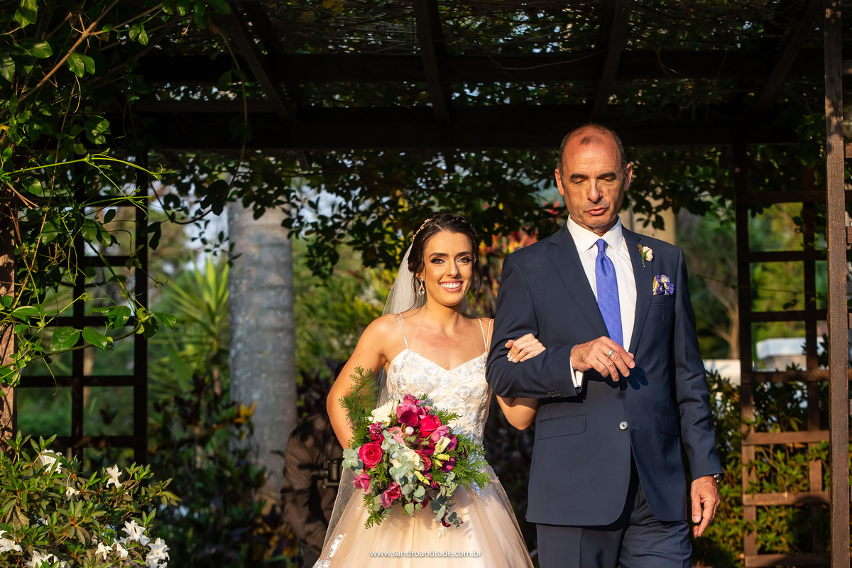O pai da noiva conduzindo sua filha até o altar, felicidade estampada no sorriso dela.