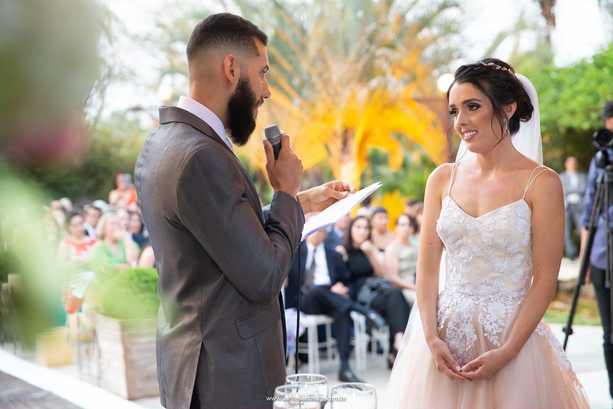 Os votos do noivo, de frente para o outro, uma fotografia colorida, muito linda, muito verde e emoção estampam essa foto.