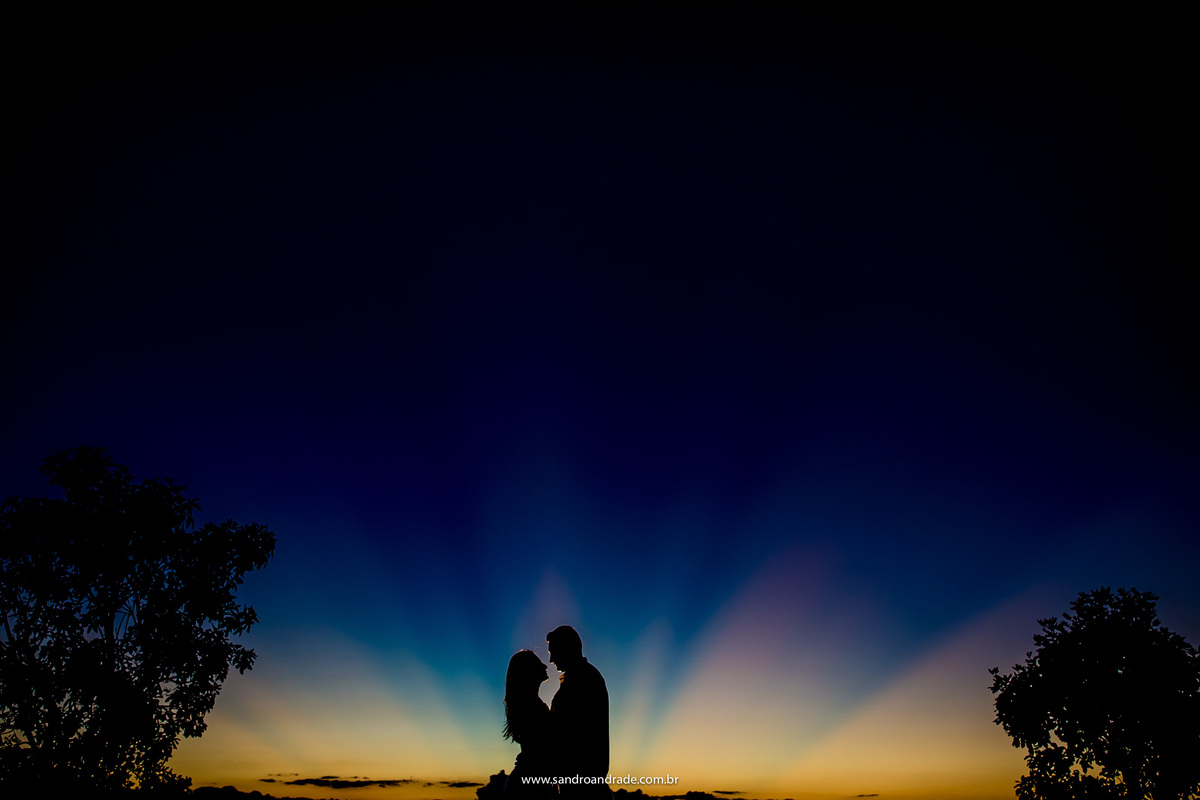 Com um lindo céu azul, desse por do sol do serrado e aquele belíssimo degradê em baixo de roxo, laranja e amarelo e o casal está em silhueta no centro da foto, arte feita pelo fotógrafo de Brasilia-DF.