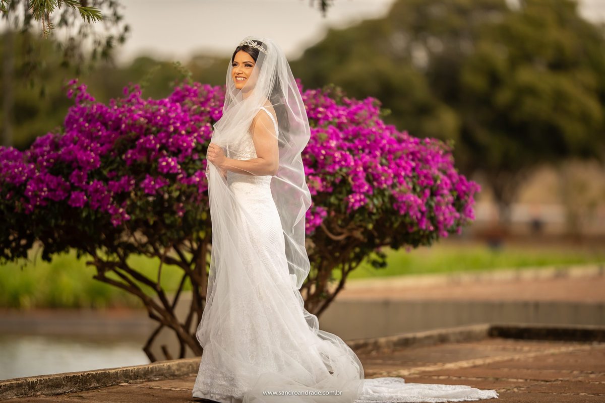 Com um belo arbustos de bougainville roxo ao fundo, Luiza posa sozinha nesta fotografia, linda e com o véu mais a frente, com ela mesma segurando, um contraste de cores e o branco de seu lindo vestido de noiva.
