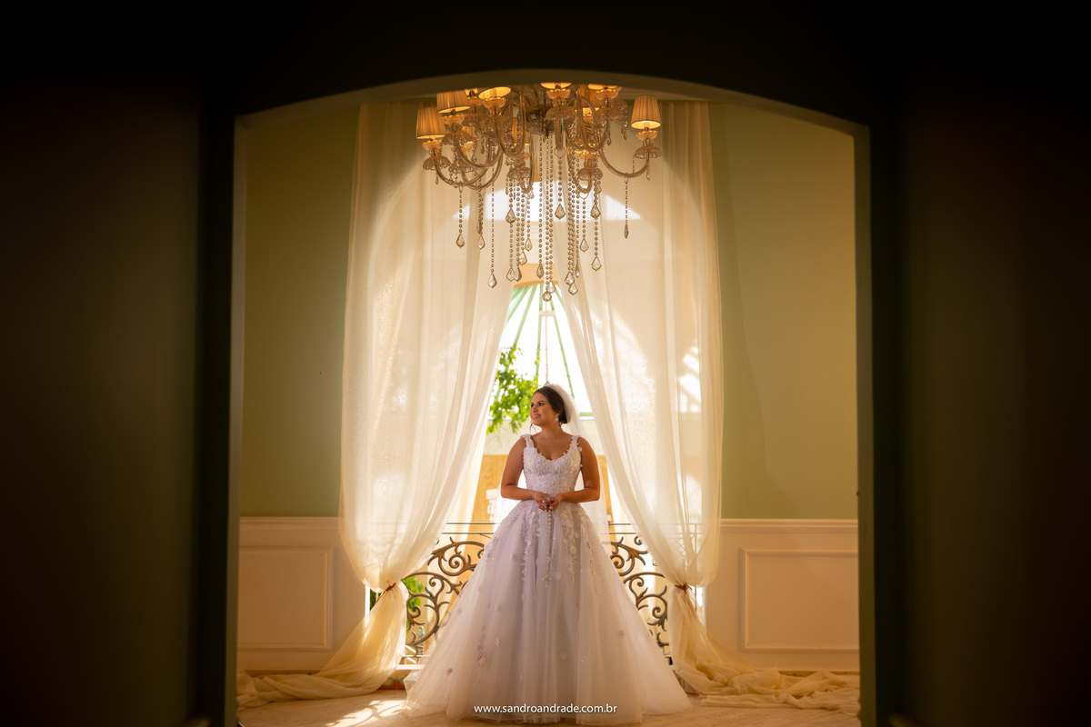 Julia parece uma princesa dentro do seu castelo, de costas para a janela que dá para o salão principal da Villa Giardini, em baixo do lustre, usando o sol como luz de contorno, Sandro Andrade fotógrafo do DF, arrasou nesta belíssima imagem colorida.