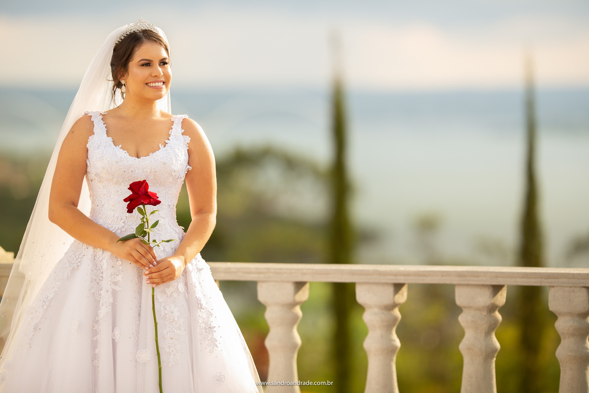 Retrato da noiva, com uma linda rosa colombiana em suas mãos e um sorriso encantador, com o giardino no fundo e o Lago Paranoá.