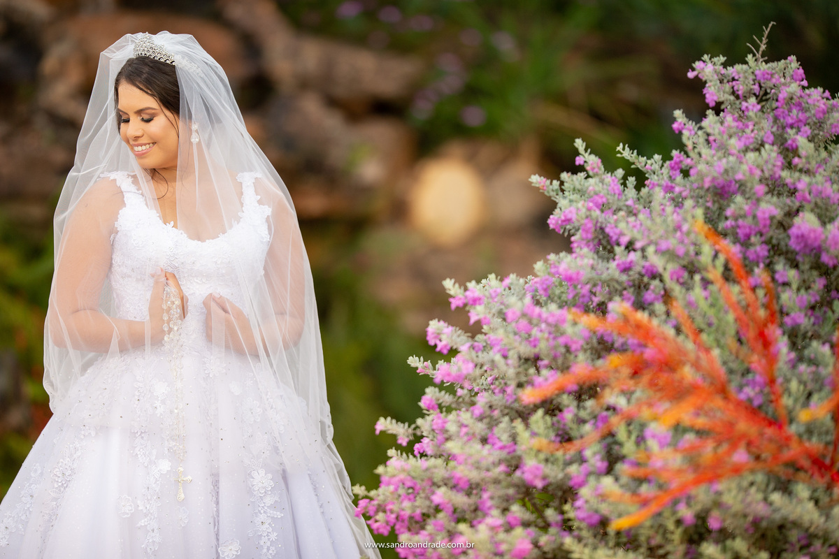 Próximo a cascata, com lindas lavandas na lateral direita, Julia segura seu véu e olha para o ombro, sorrindo e feliz.