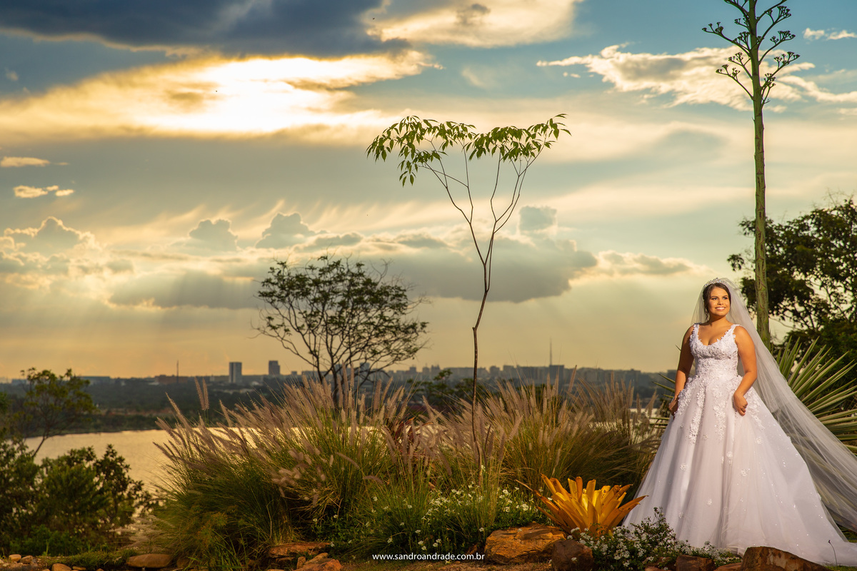 Um lindo por do sol no fundo, núvens lindas com todos os tons que podemos imaginar e a Júlia está linda, sorrindo, segurando seu vestido. A mãe da noiva está nos bastidores observando sua linda filha vestida de noiva, uma verdadeira princesa.