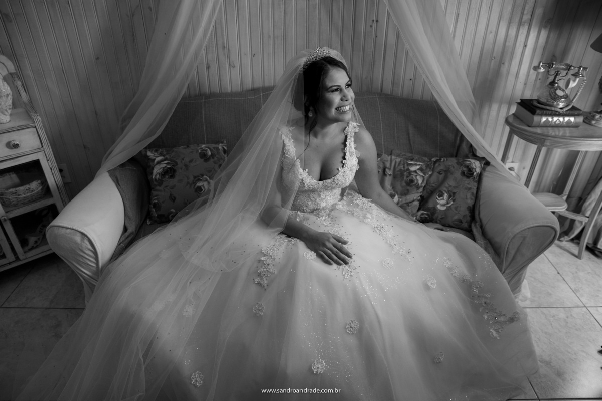 A noiva está sentada no sofá e sorrindo muito espontânea ouvindo os conselhos de sua mãe, que a acompanhou para o ensaio.