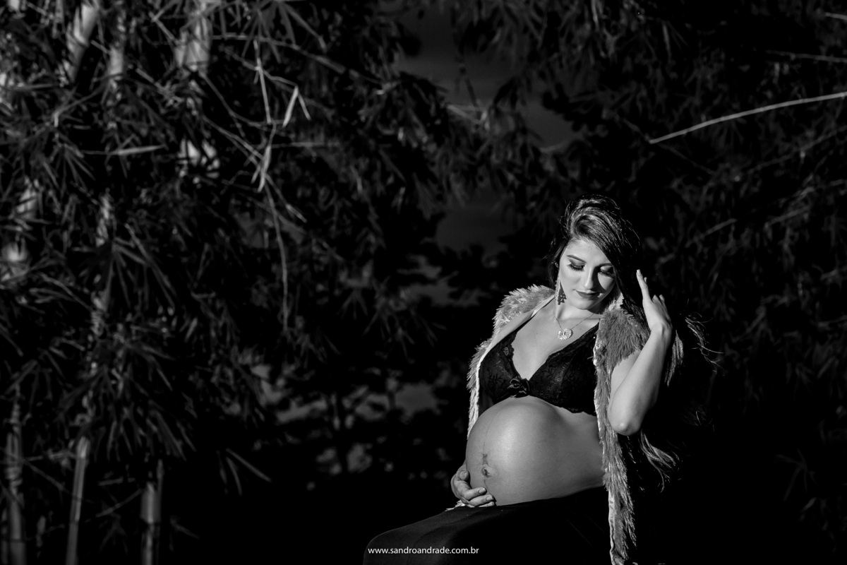 Uma linda fotografia preto e branco, a gestante está olhando para sua barriga, uma mão na barriga e a outra mão descendo pelos cabelos.