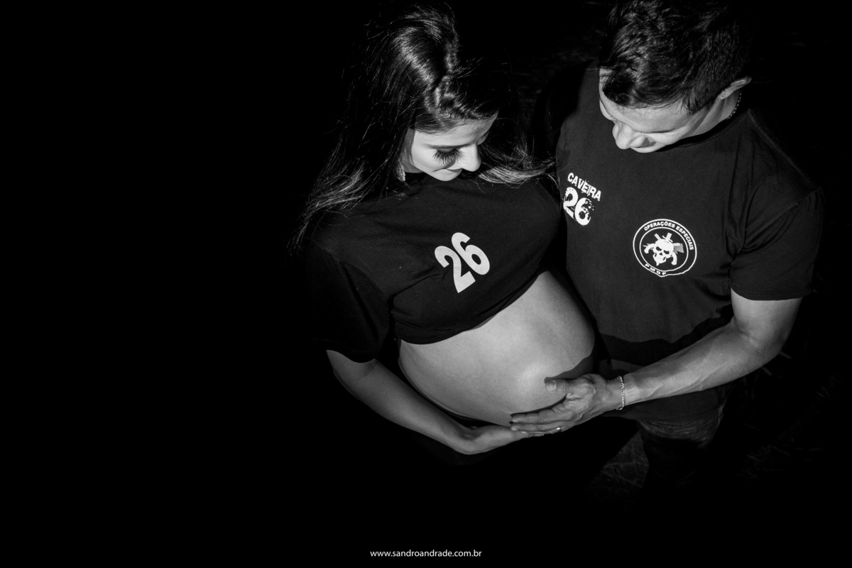 Como o papai é do BOPE, nada mais justo que ter uma foto deles vestidos na blusa da corporação, com muito orgulho esse papai veste sua camisa e olha para seu bebê dentro da barriga de sua esposa.