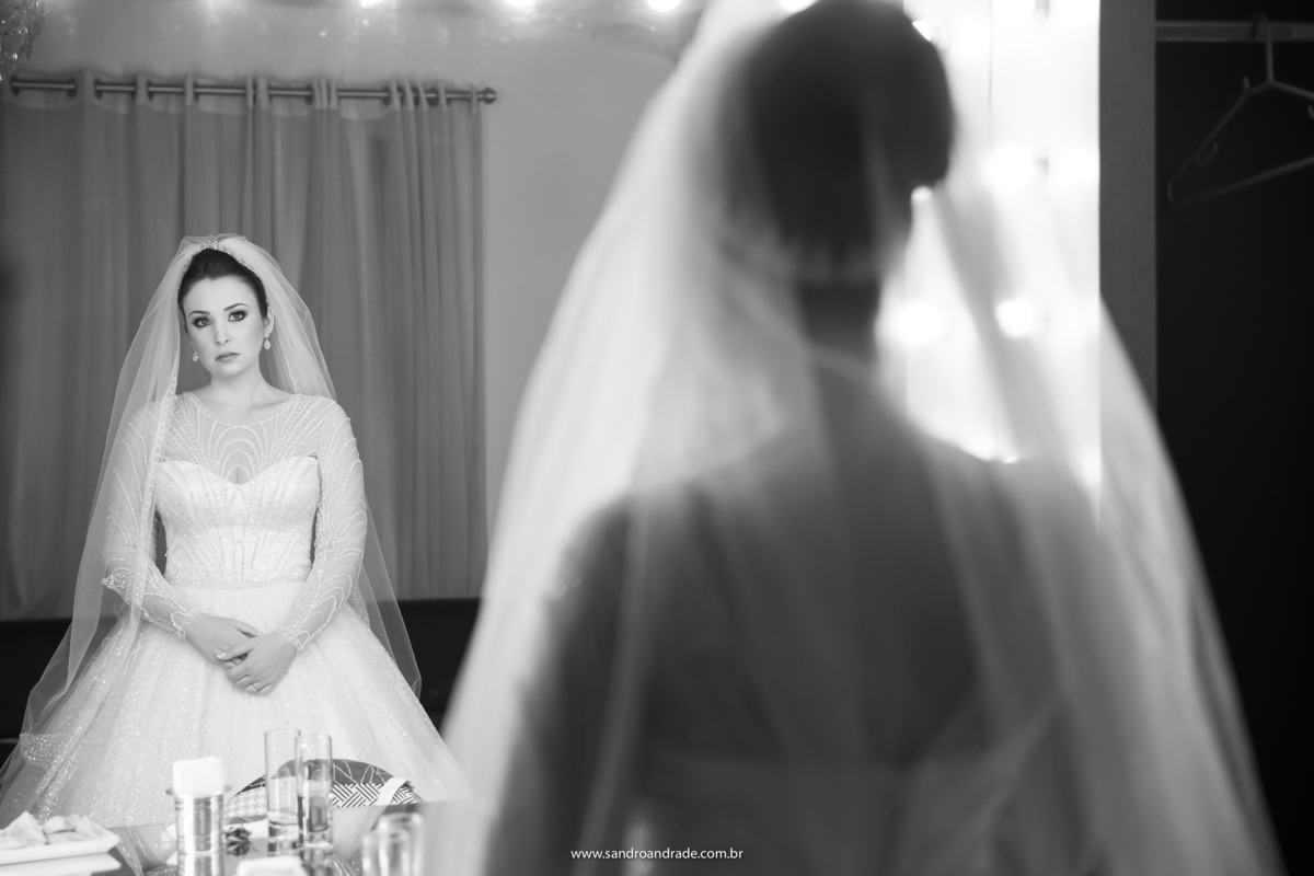 Mais uma imagem preto e branco para esta belíssima coleção, a noiva está de frente para o espelho olhando os detalhes para ver se está tudo ok com seu vestido, véu, grinalda e etc...