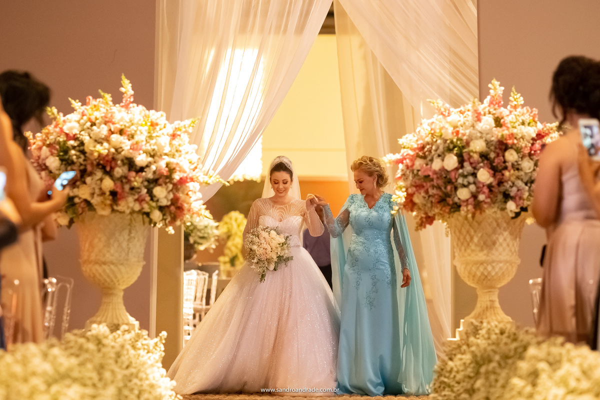 A entrada da noiva, ela entrou de mão dada com sua mãe, que está linda em um belo e elegante vestido azul bebê.