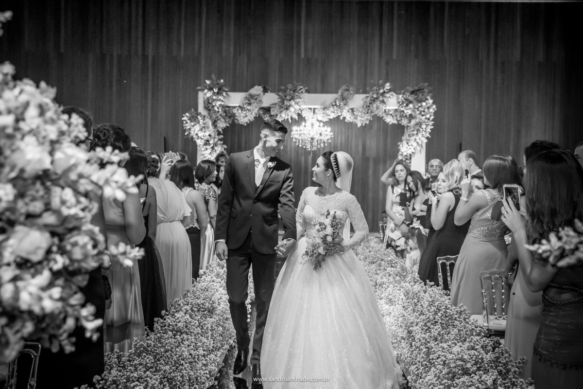 Uma fotografia mais aproximada do momento da saída dos noivos, se olhando e em preto e branco.