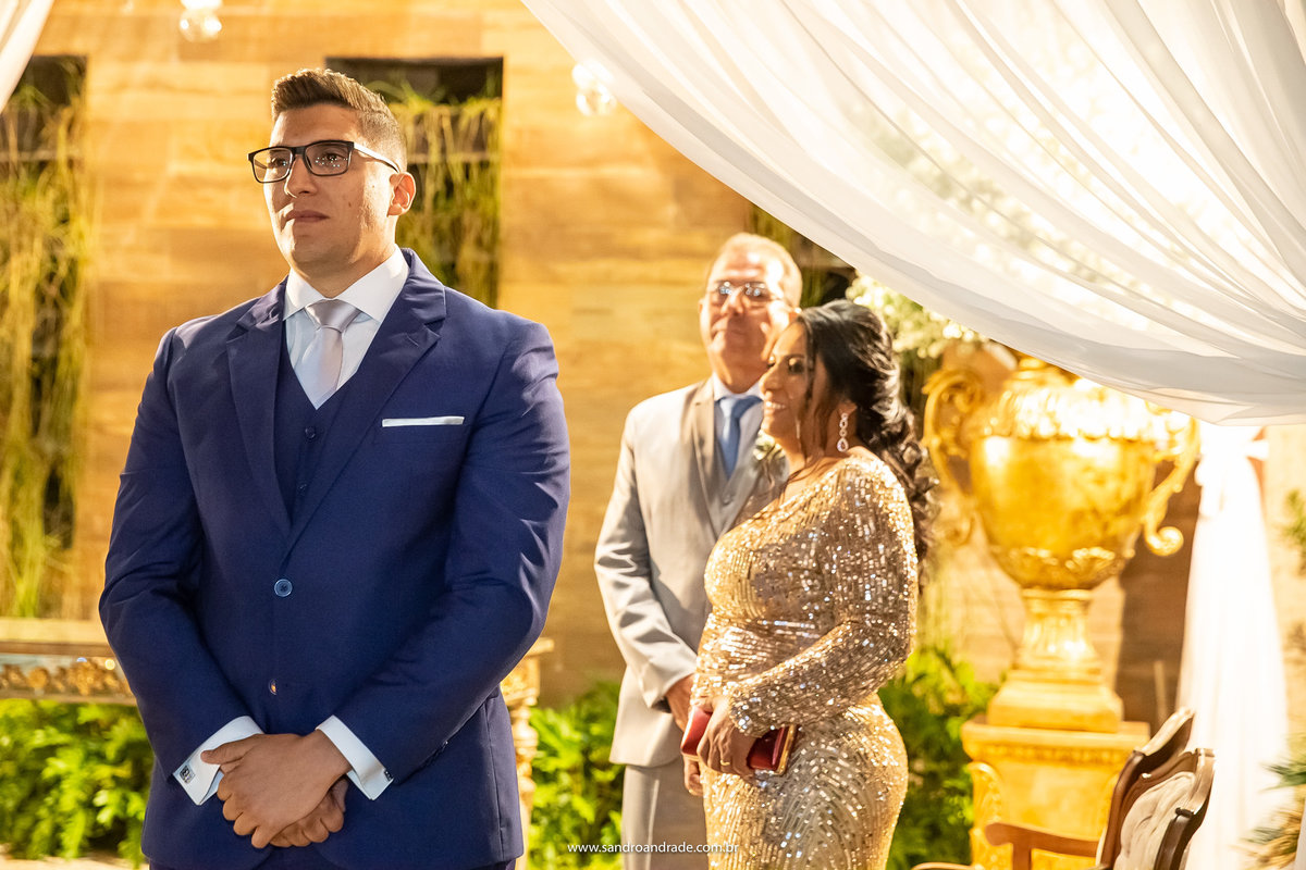 Ansioso e emocionado, Diego a espera no altar e seus pais ao fundo.
