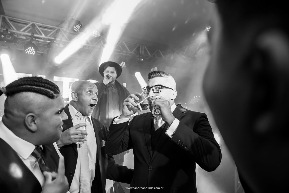 Fazendo graça, ele bebe nos dois copos de uma só vez em meio aos seus amigos.