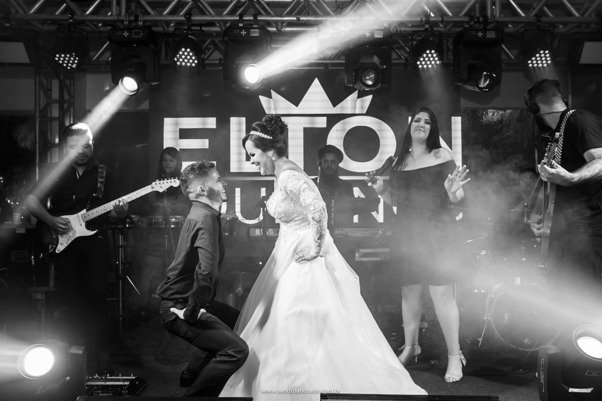 Agora no palco da banda, a noiva dança com um amigo que vai até o chão.