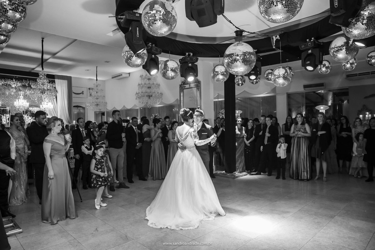 Em preto e branco o casal está ao centro da foto, dançando bem juntinhos e apaixonados.