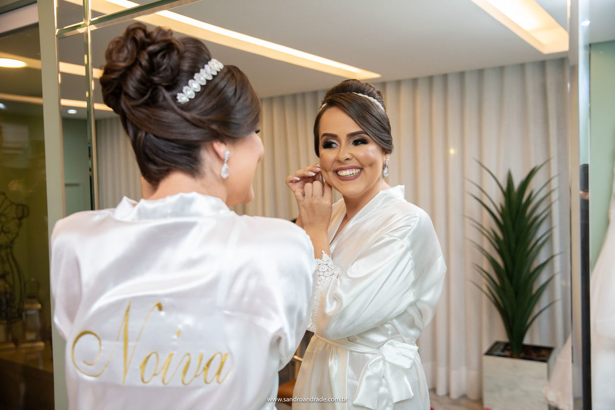 Já na suíte da noiva, ela está de frente para o espelho colocando os brincos e sorrindo.