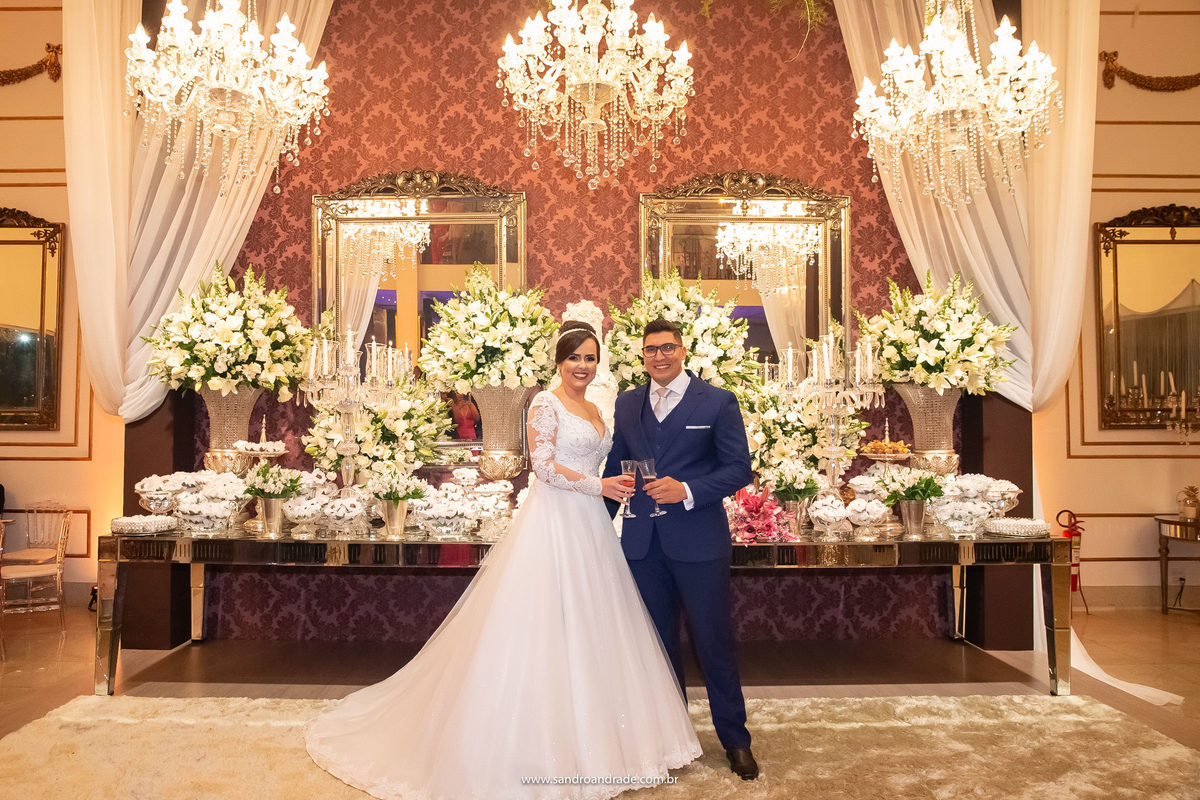 Na mesa do bolo e com a bela decoração de fundo o casal chega na festa para o famoso brinde dos noivos.