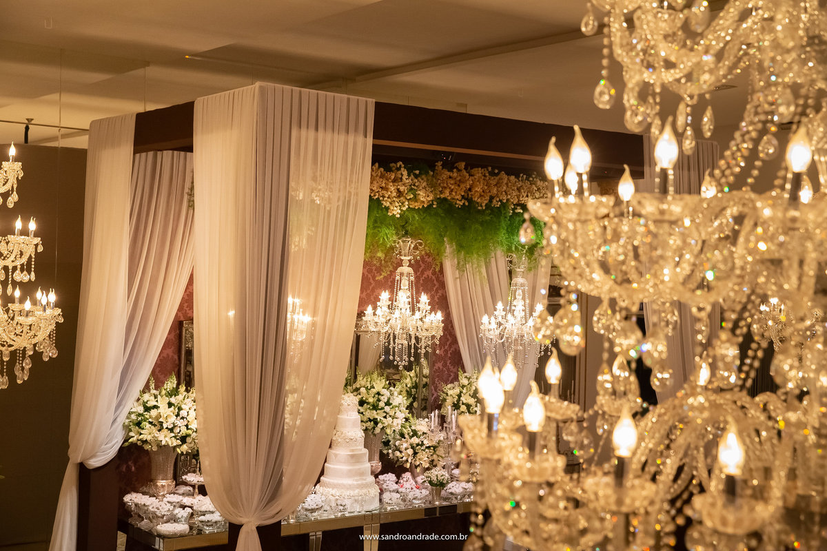 Em detalhe o lustre da casa de festa com a mesa do bolo de fundo.
