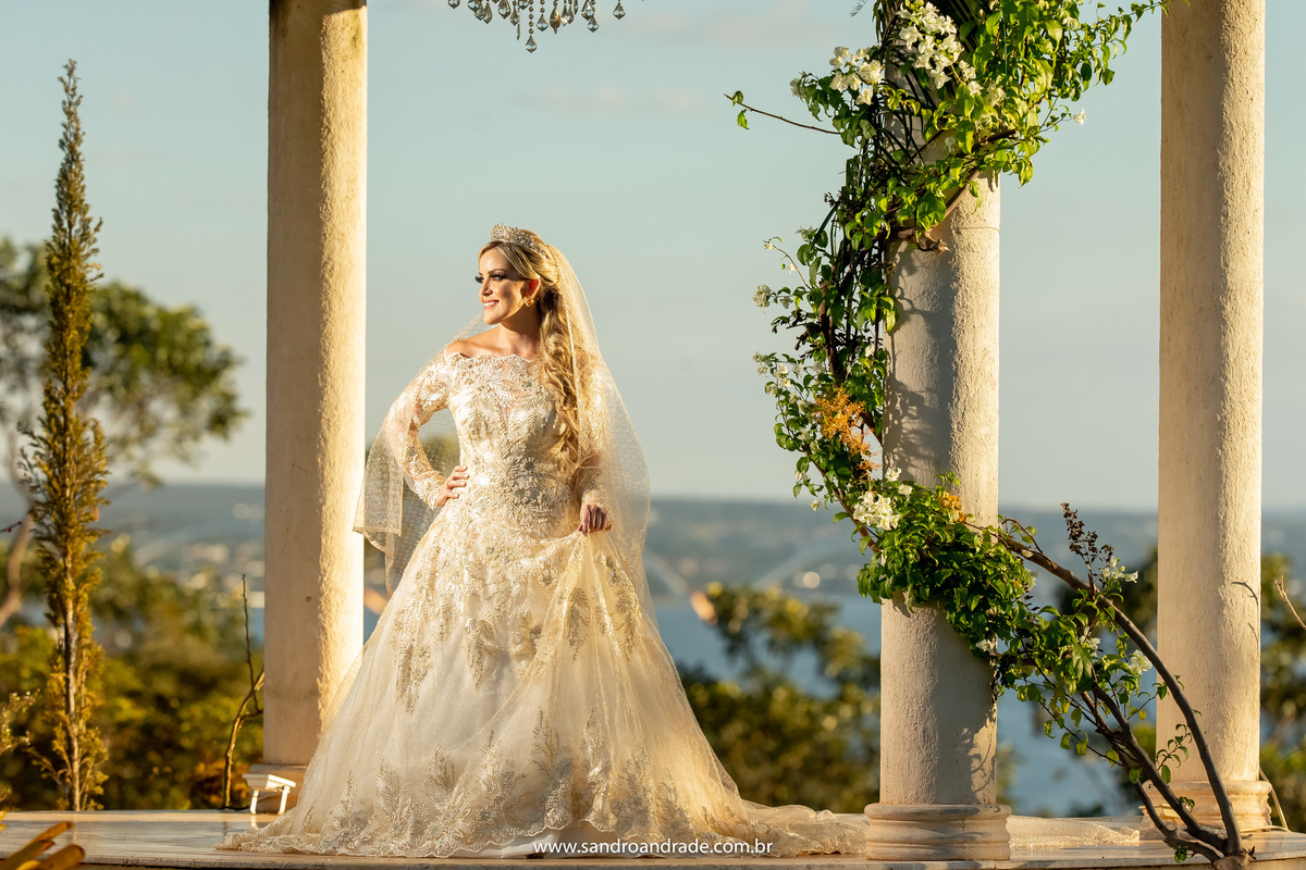 Cassia está dentro do gazebo, segurando seu vestido da Neimar Sinício Atelier.