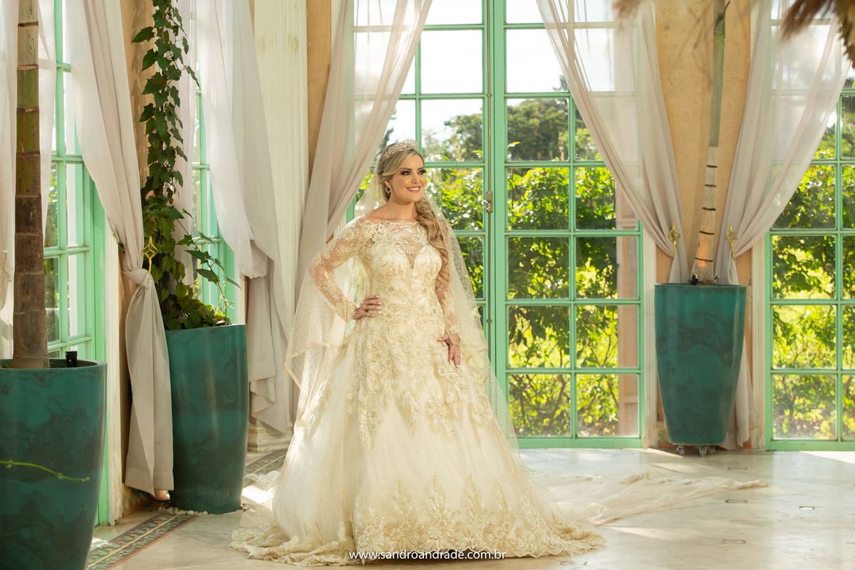 Proxima a porta lateral com uma luz do sol linda e a vegetação ao fundo, de corpo inteiro e com a mão na cintura.