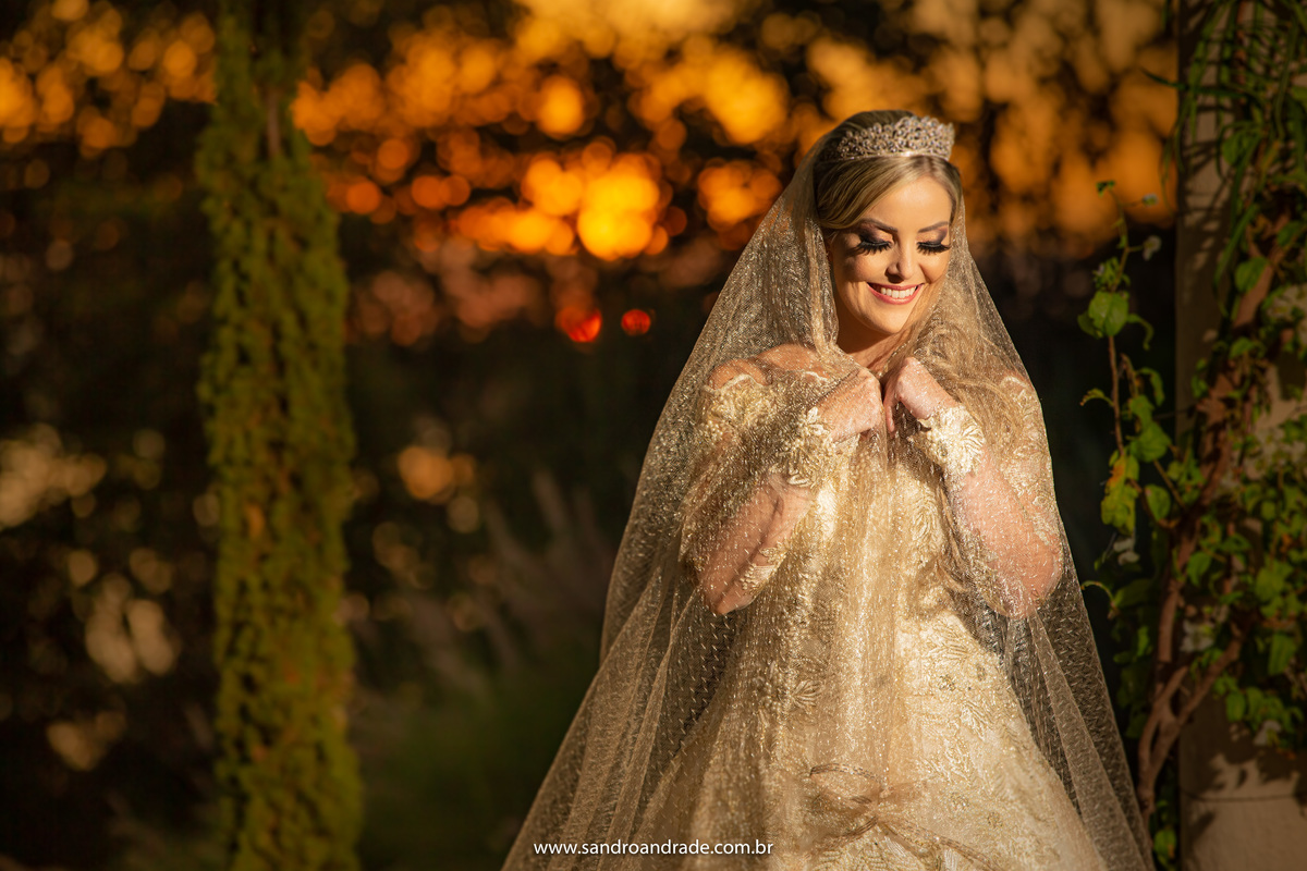 De cabeça baixa, sorrindo, feliz e segurando o véu, a noiva está maravilhosa neste retrato que finalizamos este lindo álbum.