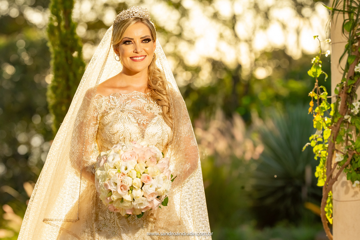 Linda foto de Cassia dentro do gazebo, muito verde fundo e uma luz linda natural que envolve todo o véu dela.