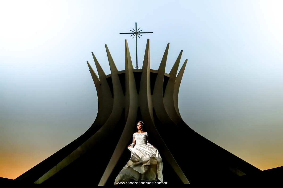 Taísa escolheu a Catedral de Brasília para finalizar seu ensaio de prévia de noiva, uma fotografia única, ela está girando com a Catedral de fundo quase toda em silhueta.
