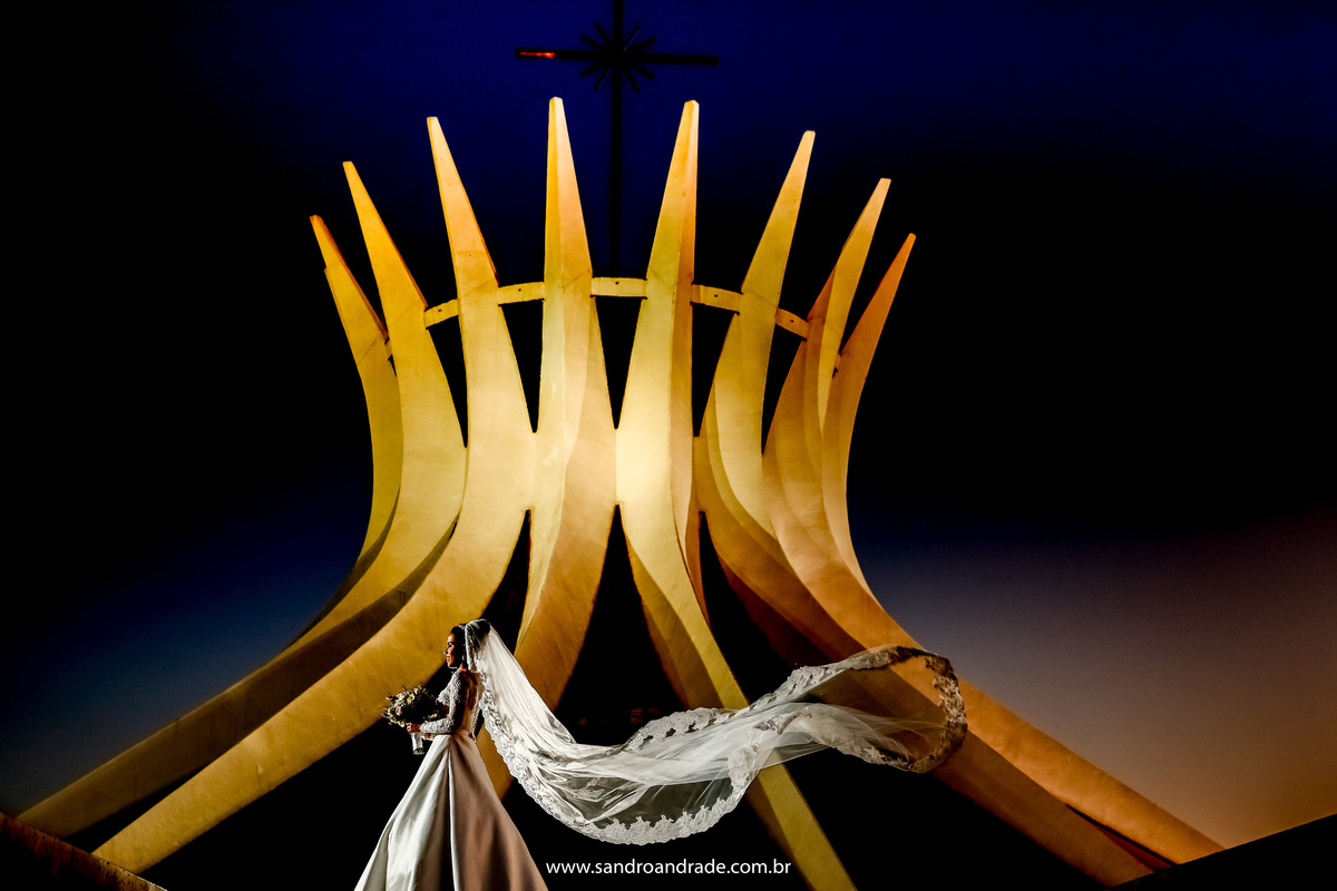 A noiva está lateralmente na com a Catedral toda  iluminada com o véu voando.