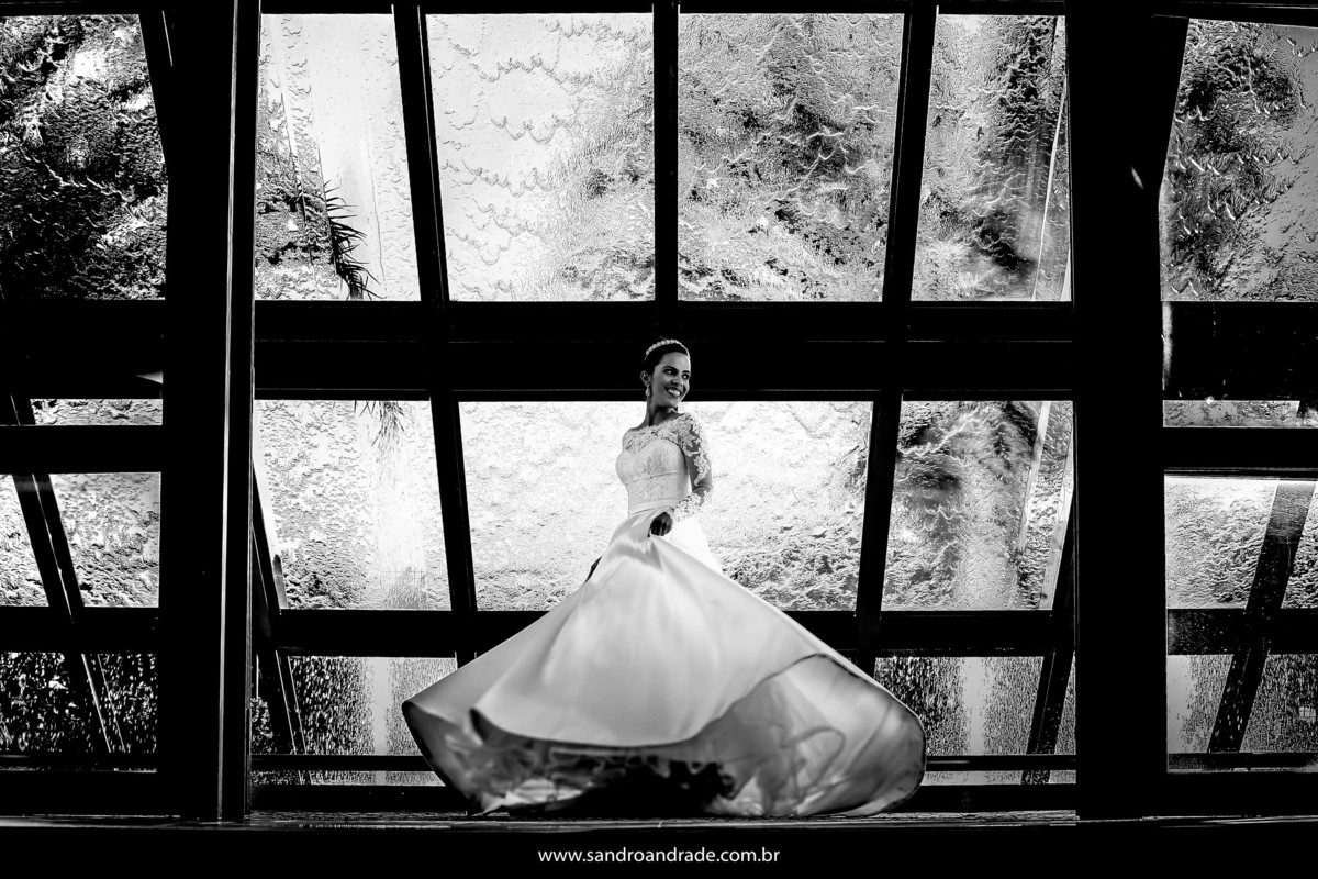 Em preto e branco girando na frente da cascata, Taísa faz um lindo movimento em seu vestido de noiva.
