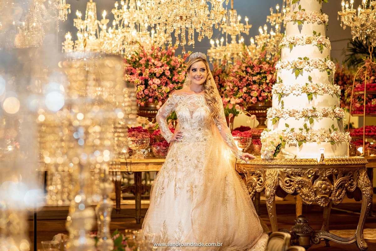 Em detalhes entre os cristais, Cassia está ao lado da mesa do bolo, sorrindo para Sandro Andrade seu fotógrafo de casamento premiado e artista das cores e composição.